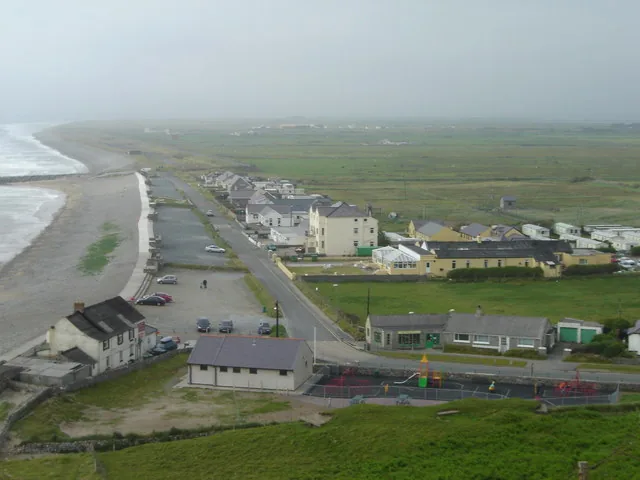 An elevated view of Dinas Dinlle's seafront, houses and beach in one frame, looking down from the hillfort.