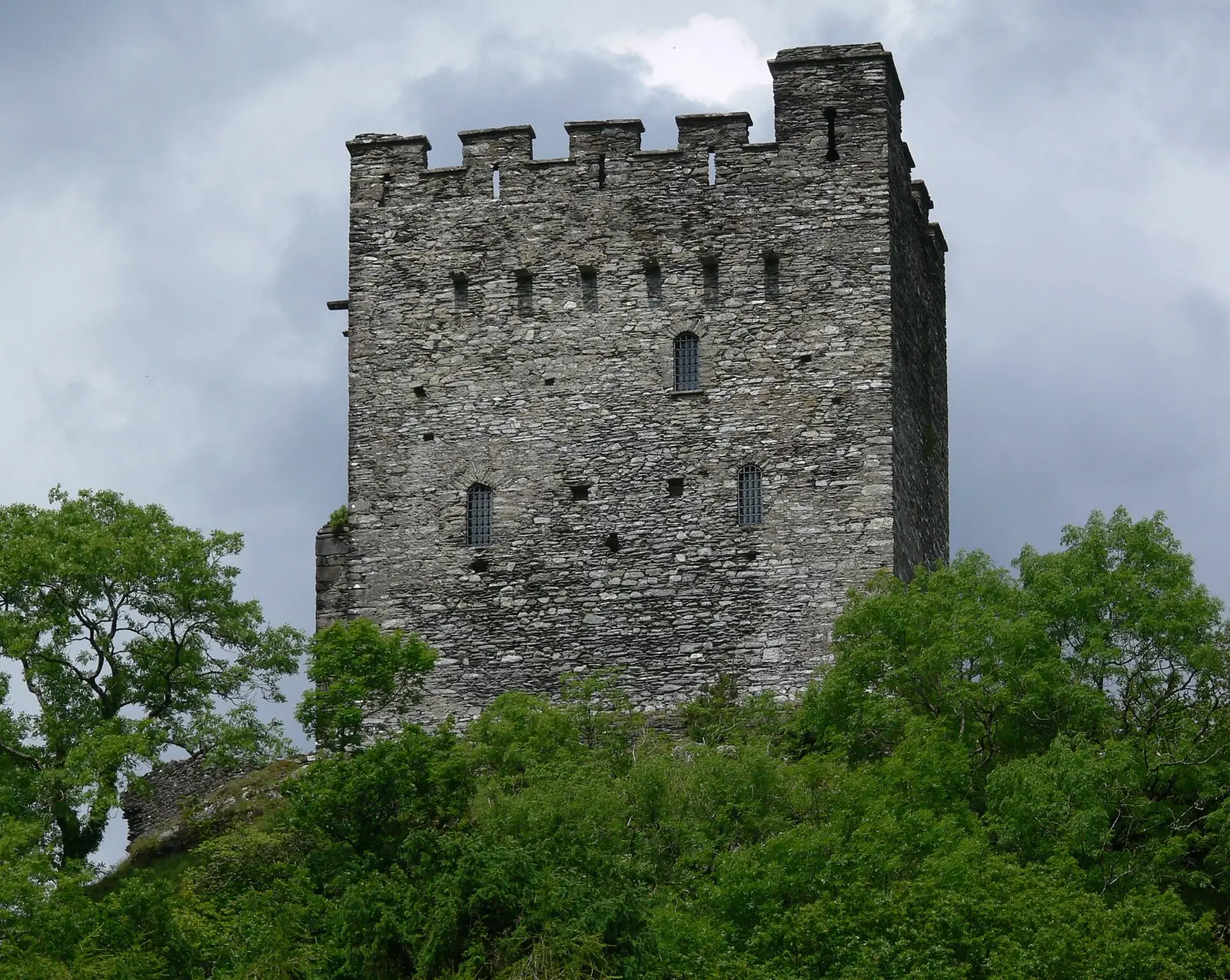 The keep of Dolwyddelan Castle, its battlemented top stage rising above trees on the rock