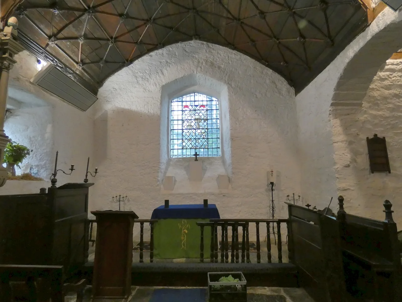 Inside St Gwyddelan's Church, a whitewashed barrel-roofed chancel with a small stained-glass window above the altar