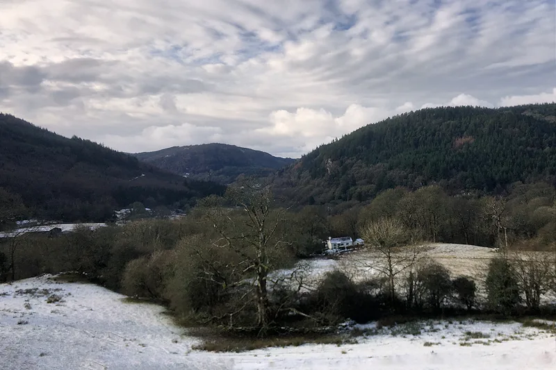 A snow-covered valley near Fairy Glen in winter, with a distant farmhouse among bare trees.