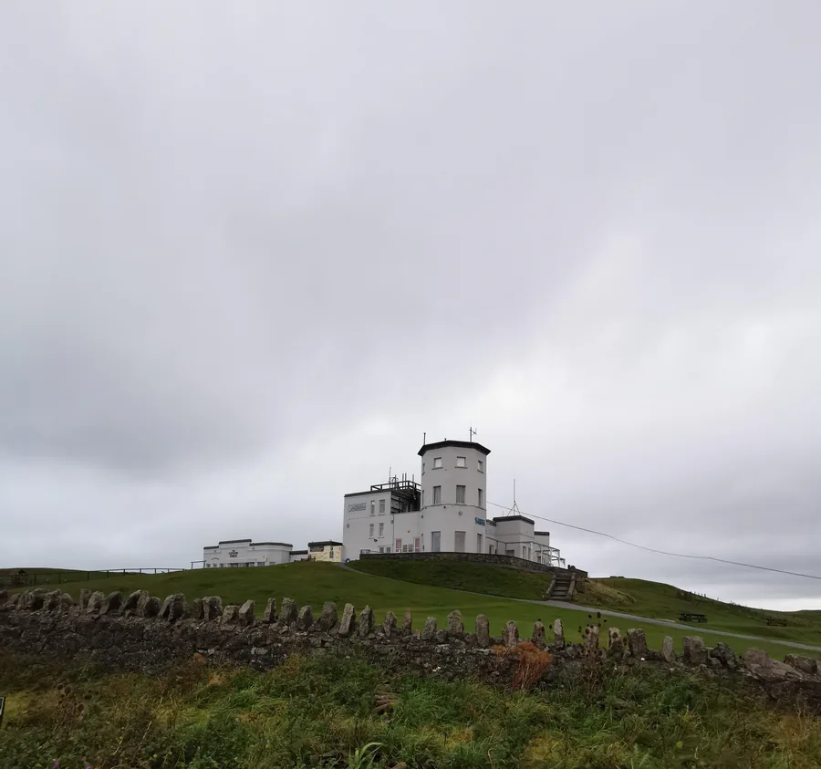 The Great Orme Summit Complex on its grassy hilltop above Llandudno, seen from below an old stone wall.