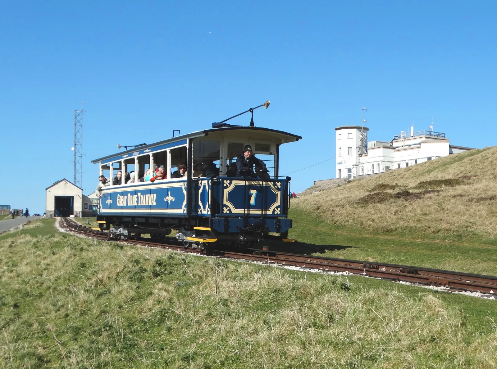 Great Orme Tramway car number 7, carrying passengers up the grassy hillside towards the Summit Complex.