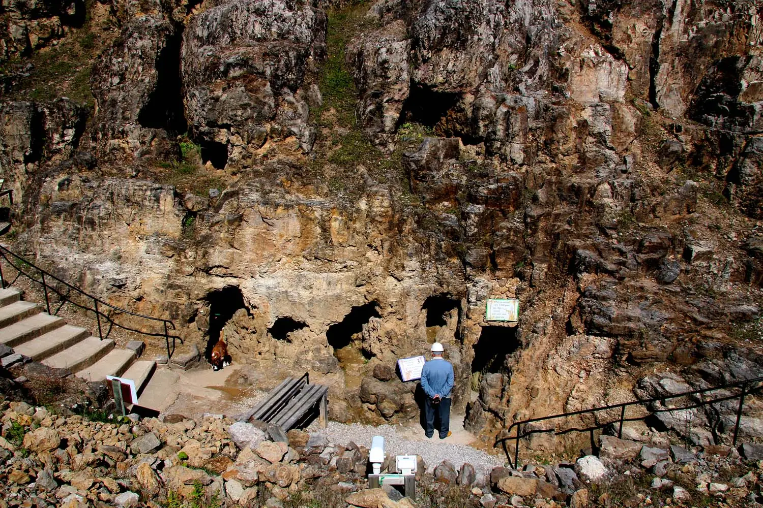 The rock-cut entrances to the underground Bronze Age copper mines on the Great Orme, with a visitor and guide below the cliff face.
