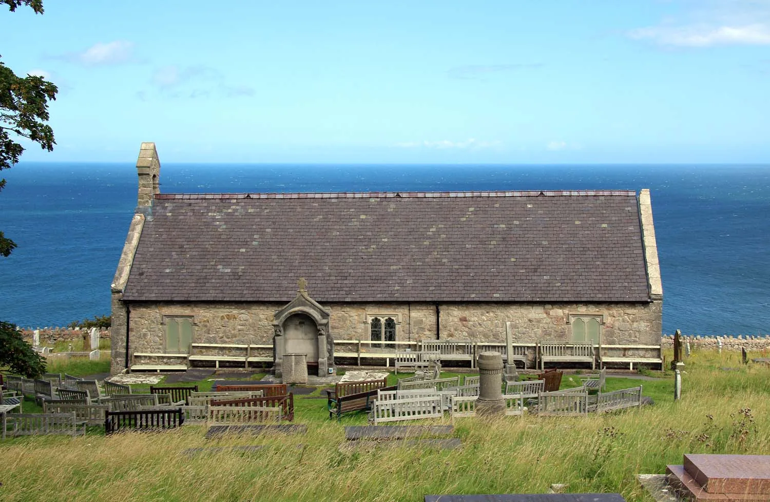 St Tudno's Church, a stone building with a slate roof, standing in its clifftop churchyard above the sea.