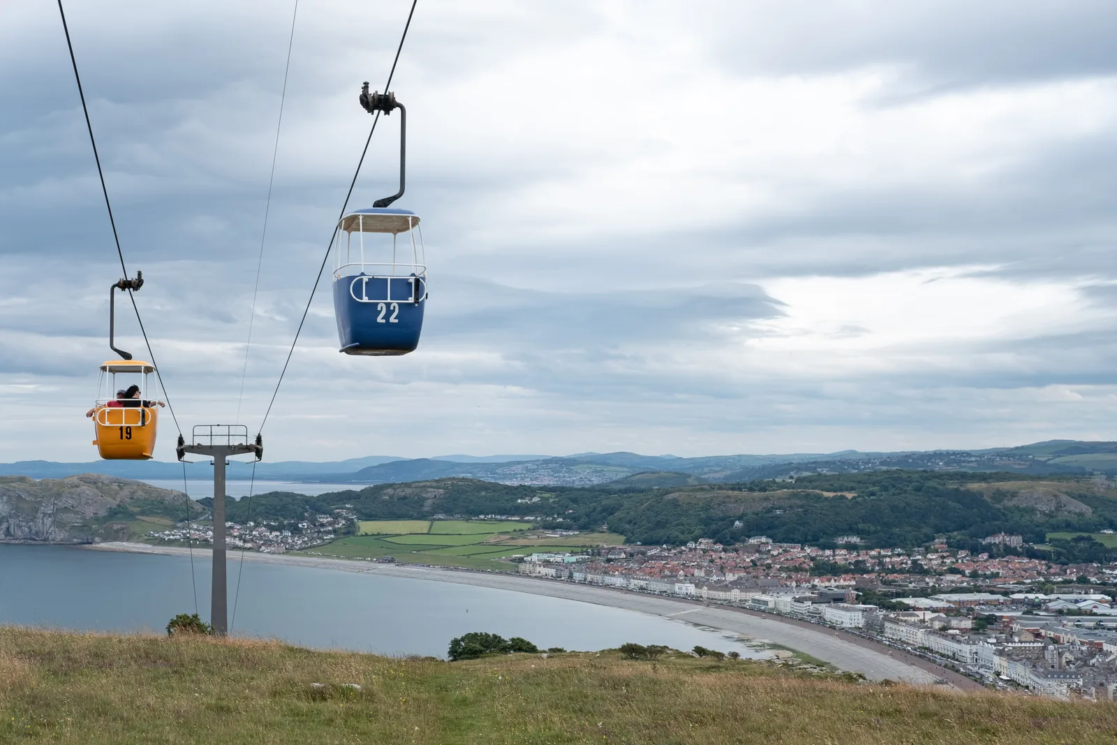 Two Great Orme Cable Car cabins crossing above Llandudno's beach and North Shore promenade.