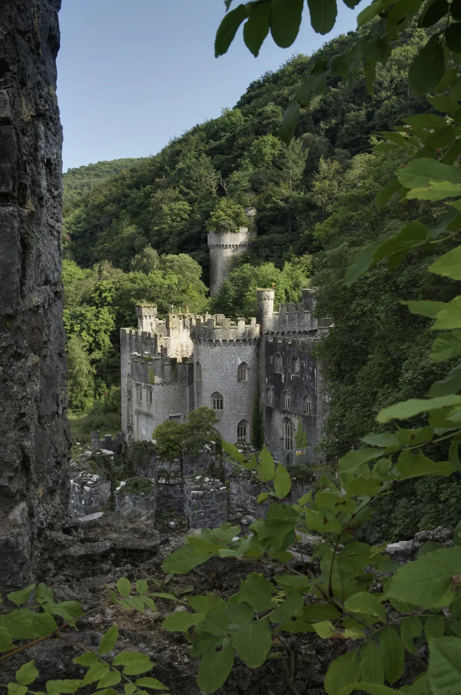 Gwrych Castle's turreted Gothic Revival exterior seen through woodland foliage above Abergele.