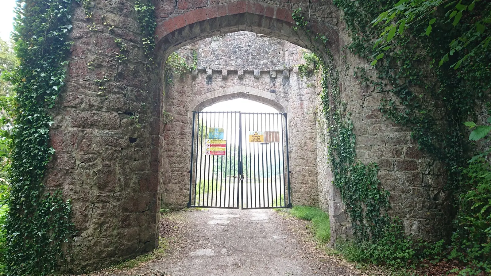 An ivy-covered stone gateway arch at Gwrych Castle, with a metal gate across the drive.
