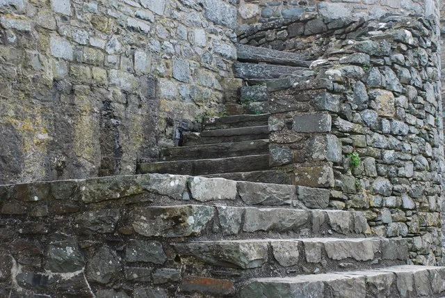 Worn stone and timber steps set into a castle wall at Harlech Castle, moss growing on the weathered masonry.