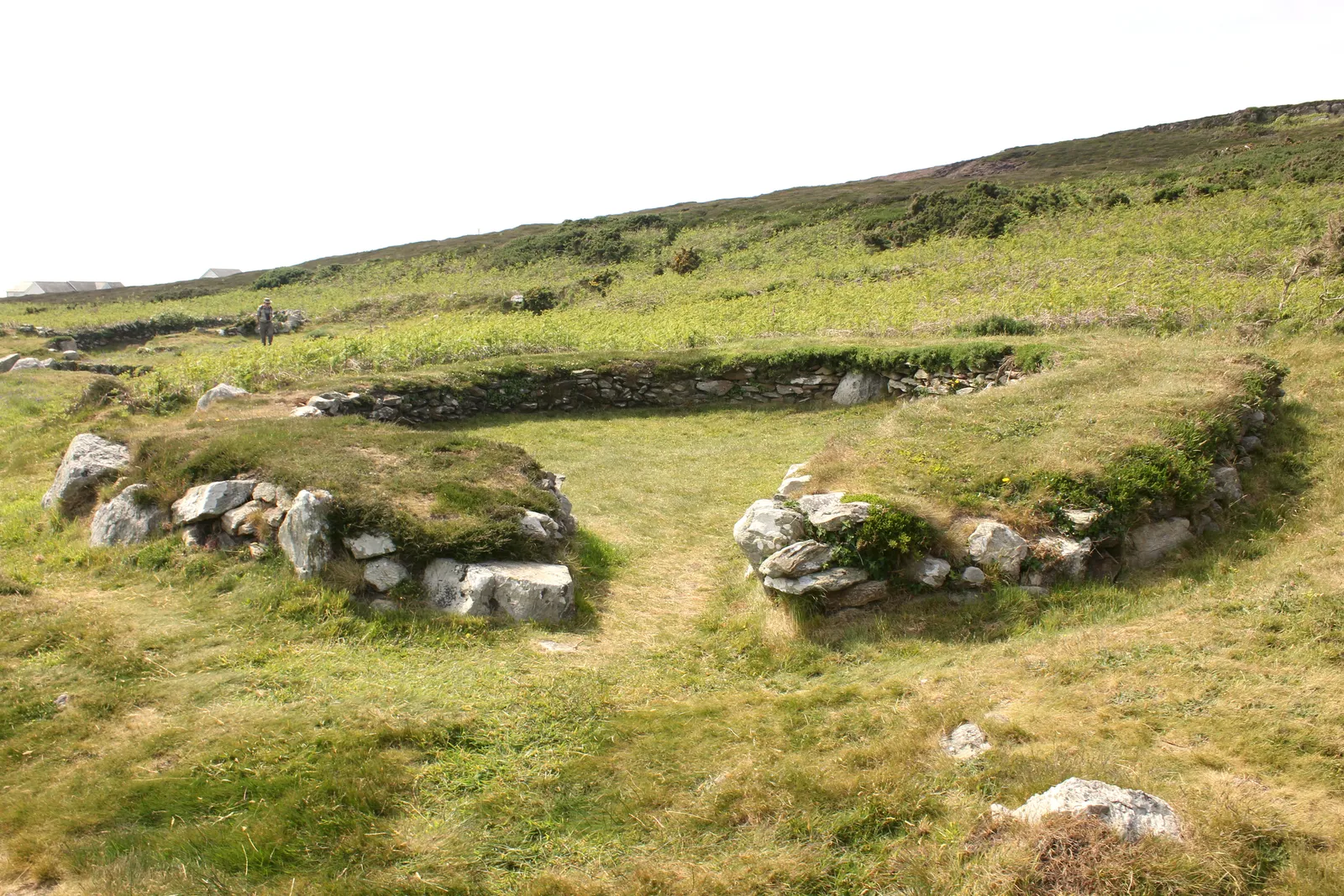Iron Age hut circles on the slopes of Holyhead Mountain — the low stone walls of the ancient settlement below the summit, with the mountain ridge above.