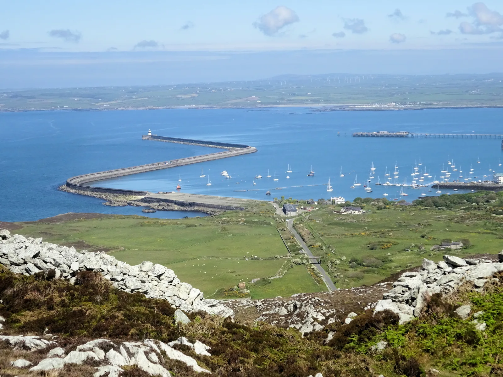 Holyhead seen from the summit of Mynydd Twr: the long curving breakwater, the marina full of moored yachts, the ferry port and the town spread along the shore below.