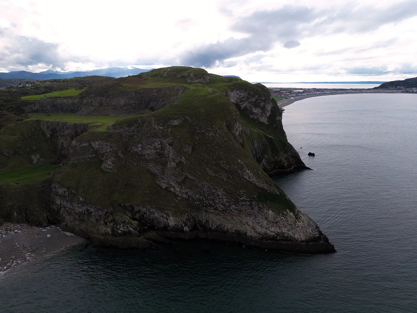 An aerial view from the sea of the Little Orme headland, showing its limestone cliffs, Angel Bay's cove, and Llandudno Bay beyond.