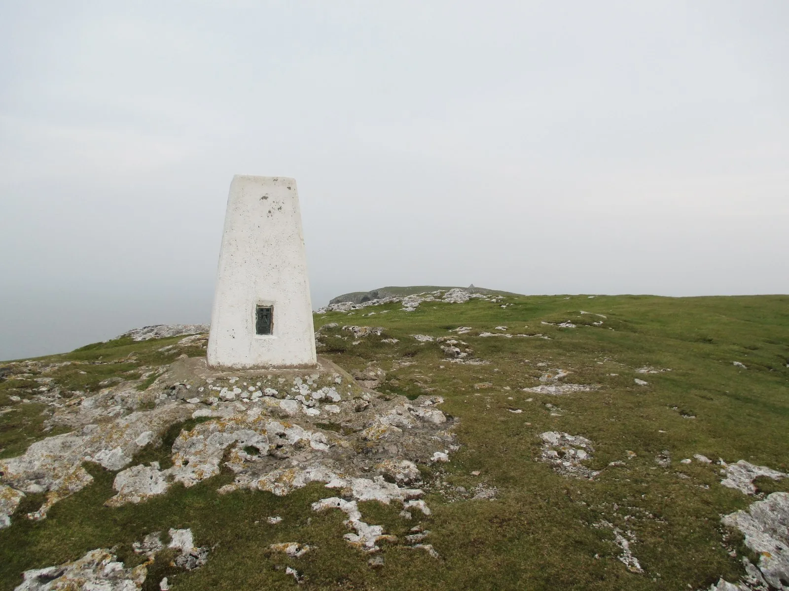 The Ordnance Survey trig pillar on the higher summit of the Little Orme, with the coastline stretching away behind it.