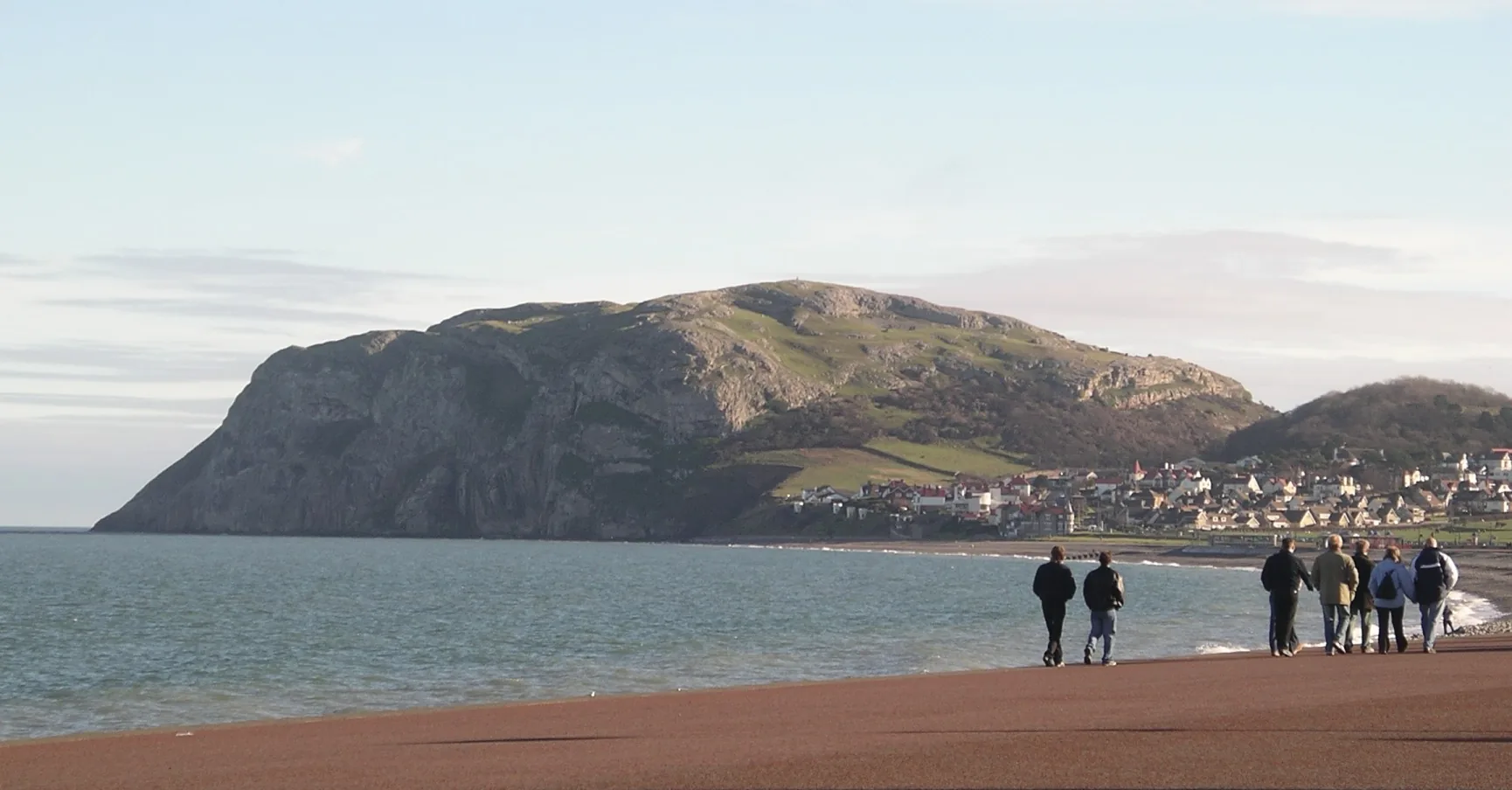 A limestone headland rising from the sea above the beach and seafront at Llandudno on the north coast of Conwy, walkers on the shore, the town gathered at the foot of the cliffs.