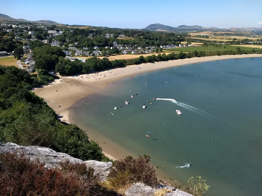 Llanbedrog beach and village seen from Mynydd Tir-y-Cwmwd, the sand curving away below wooded slopes on the Llŷn Peninsula, Gwynedd.