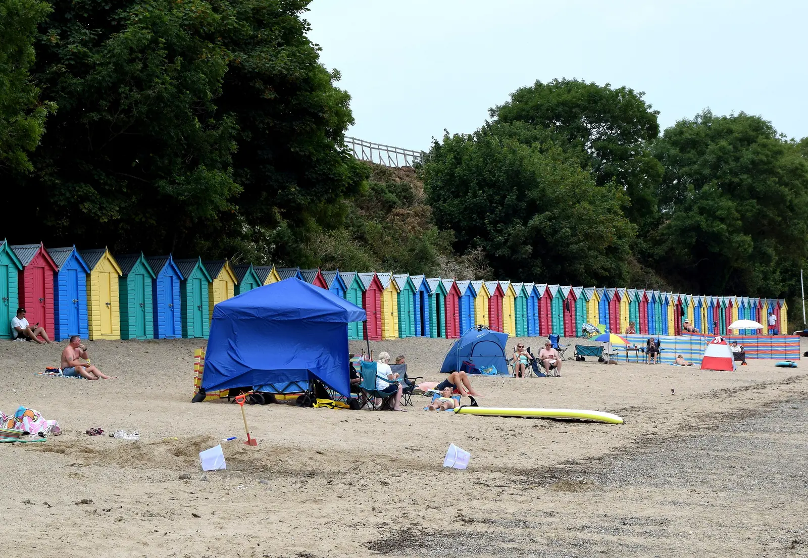 Llanbedrog&rsquo;s beach huts along the back of the sand, with windbreaks and people on the beach in front