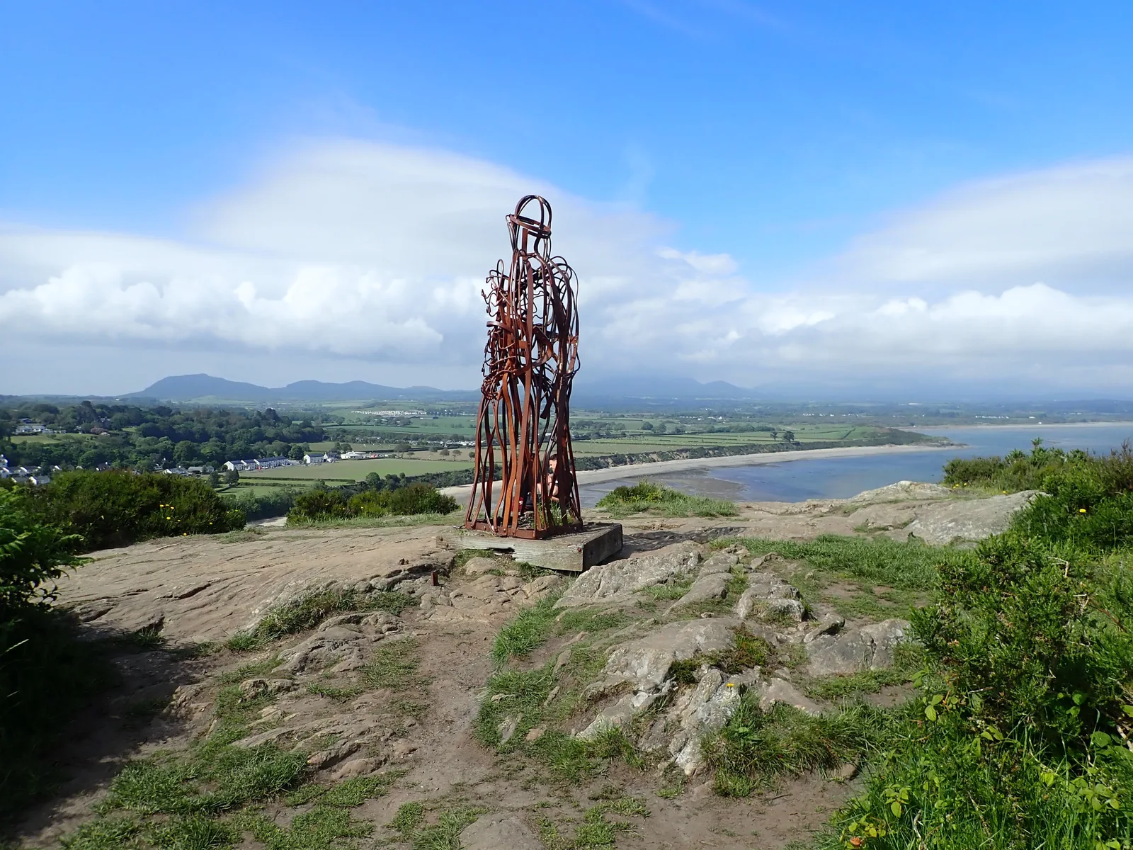 The Tin Man sculpture on the headland above Llanbedrog, the bay and the hills of Llŷn spread out behind it