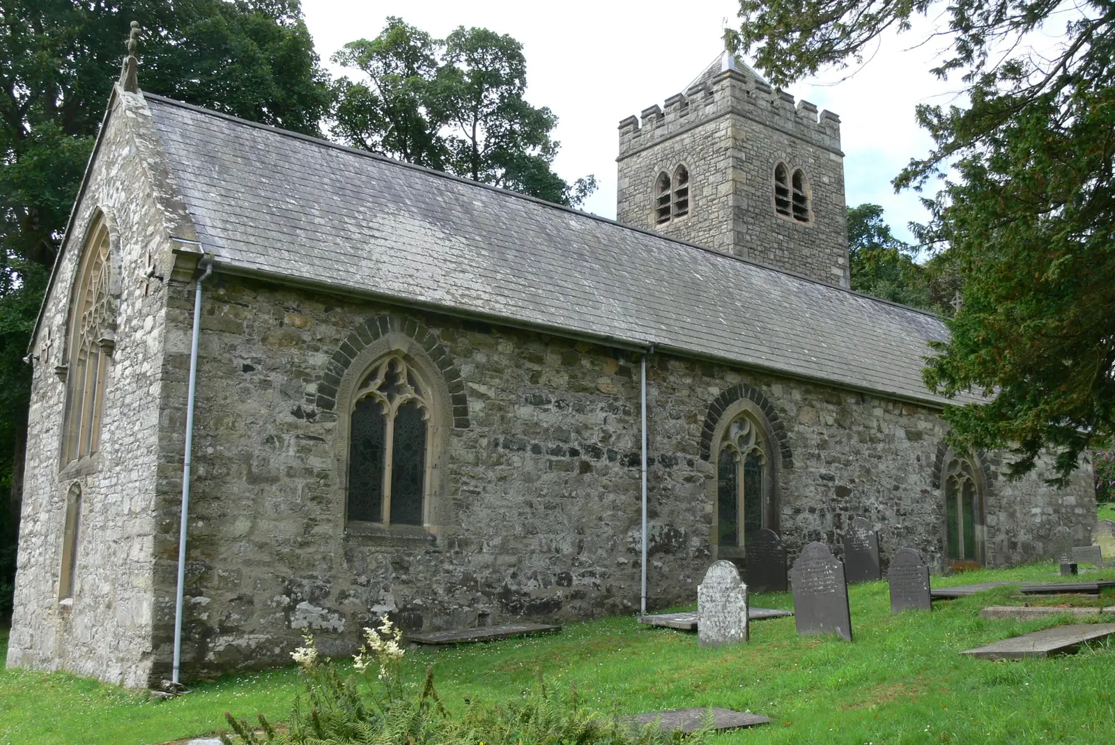 St Pedrog&rsquo;s Church, Llanbedrog: a low stone nave and battlemented tower above its graveyard