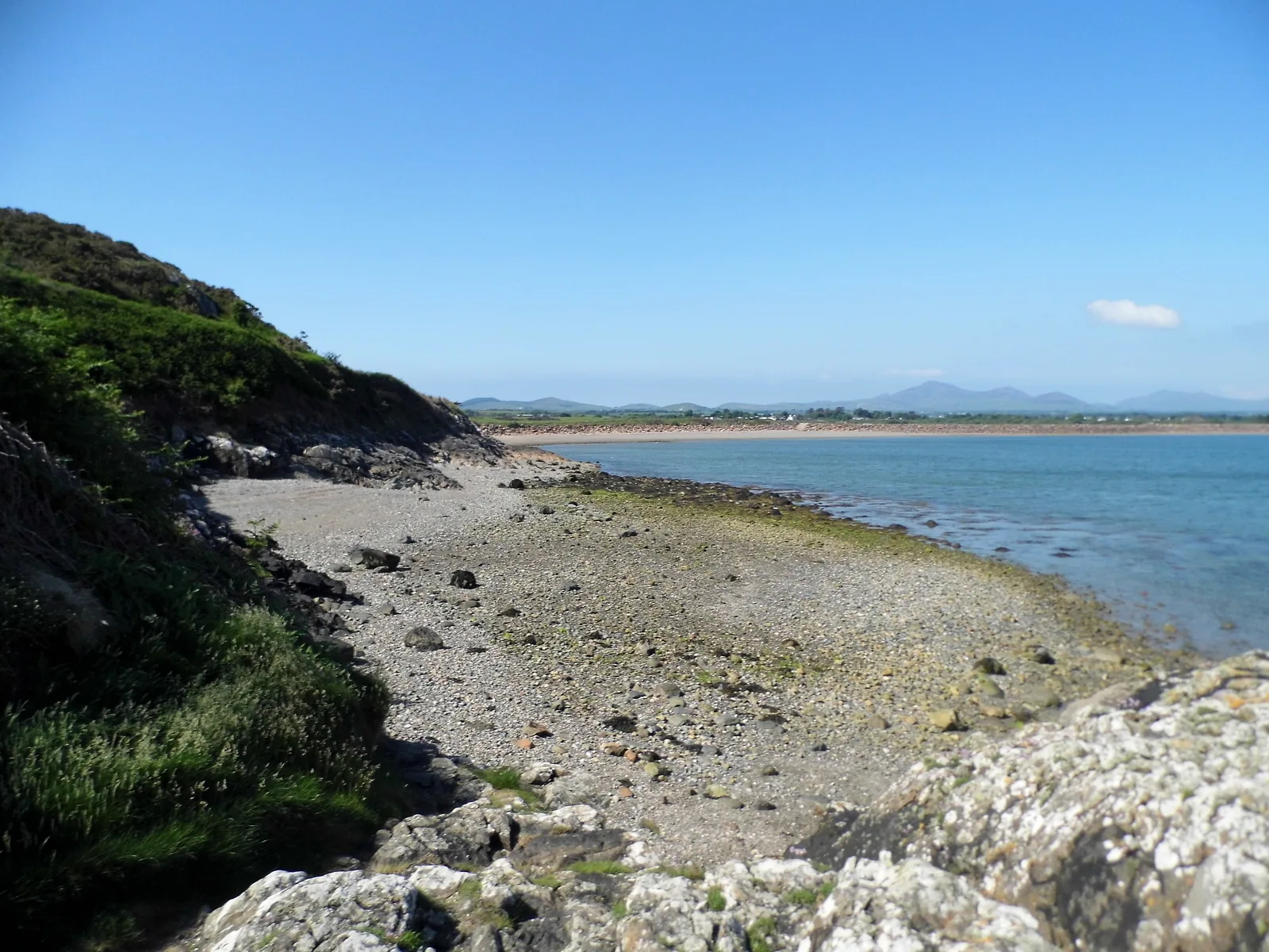 The shingle and rock shore at Carreg y Defaid, looking back along Llanbedrog&rsquo;s sand towards the Llŷn hills