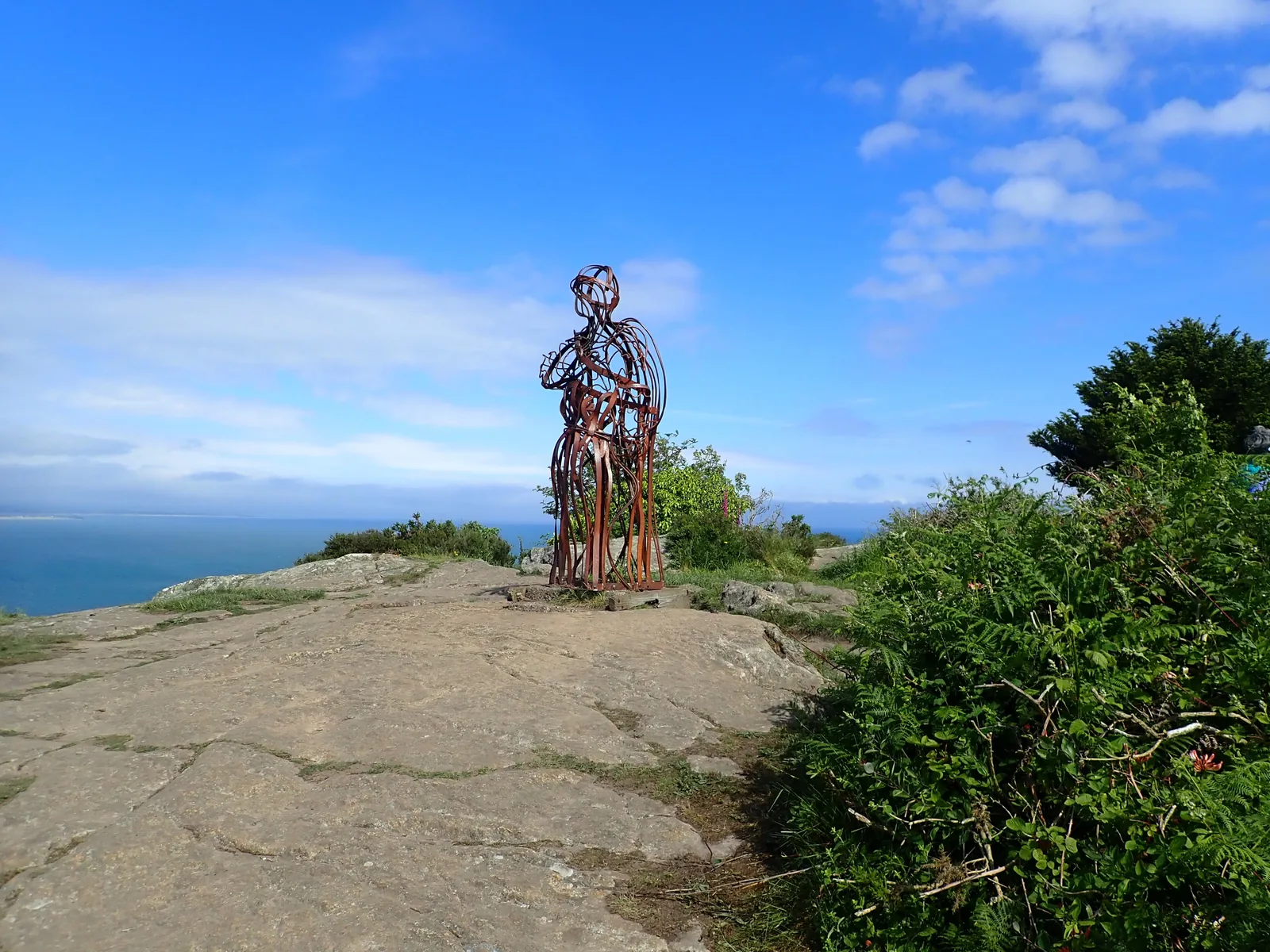 The Tin Man, a figure of curved metal bars, standing on bare rock above the sea on Mynydd Tir-y-Cwmwd