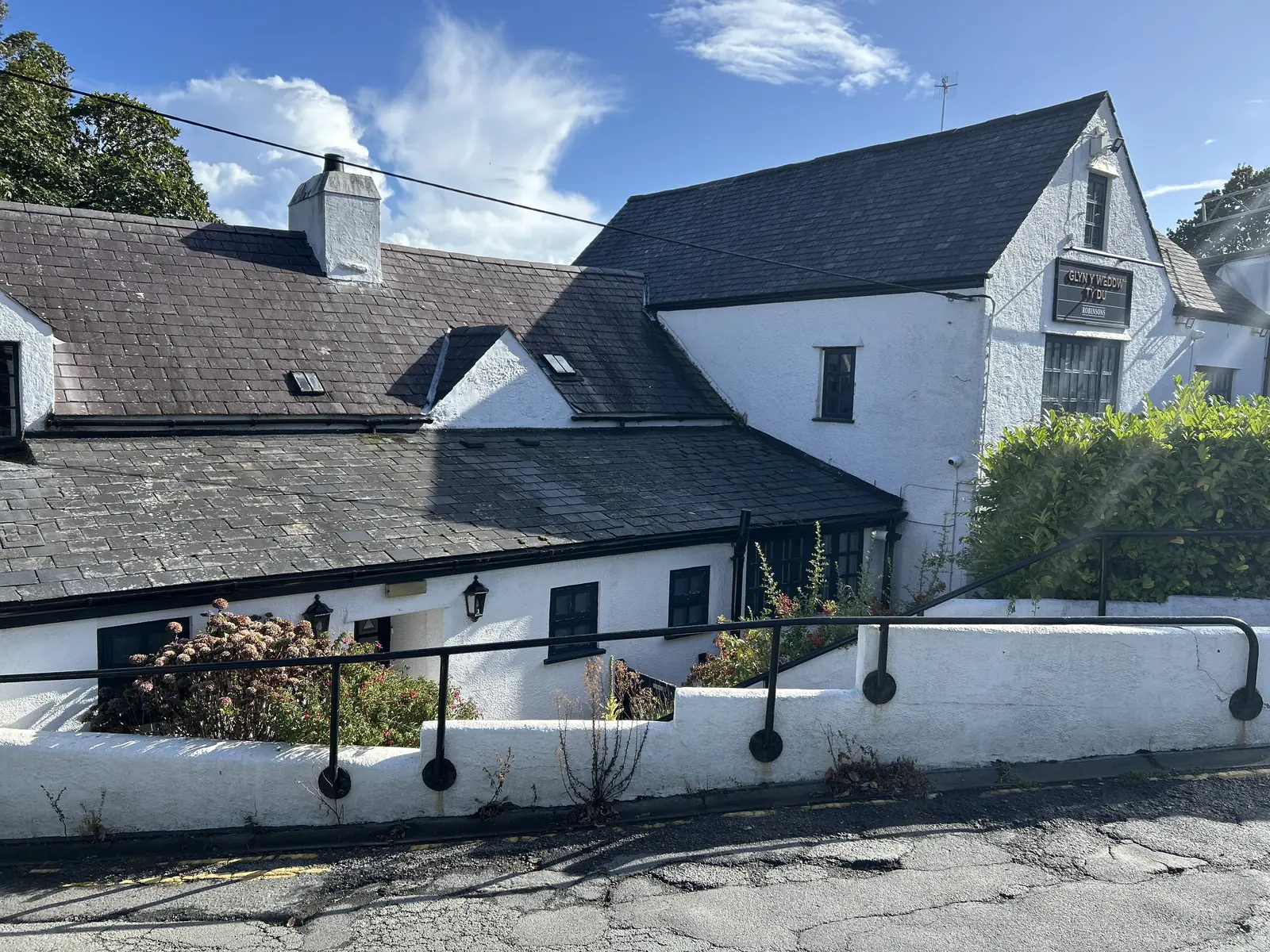 A whitewashed slate-roofed pub and its low walled forecourt at the top of the village in Llanbedrog
