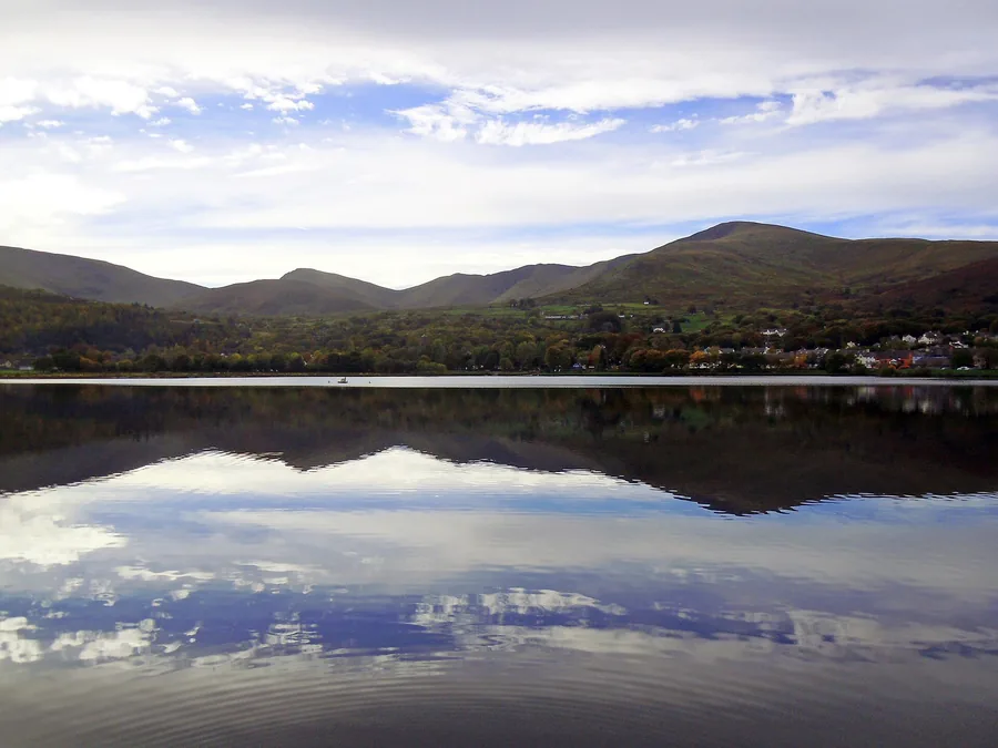 Llyn Padarn's still water reflecting Llanberis village and the mountains of Eryri behind it.