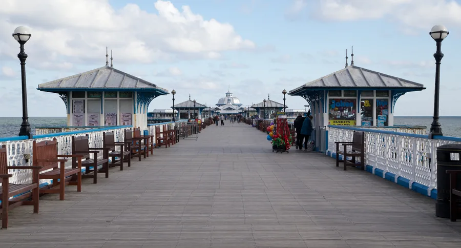 Looking along the deck of Llandudno Pier, its white ironwork and kiosks receding towards the pier head.