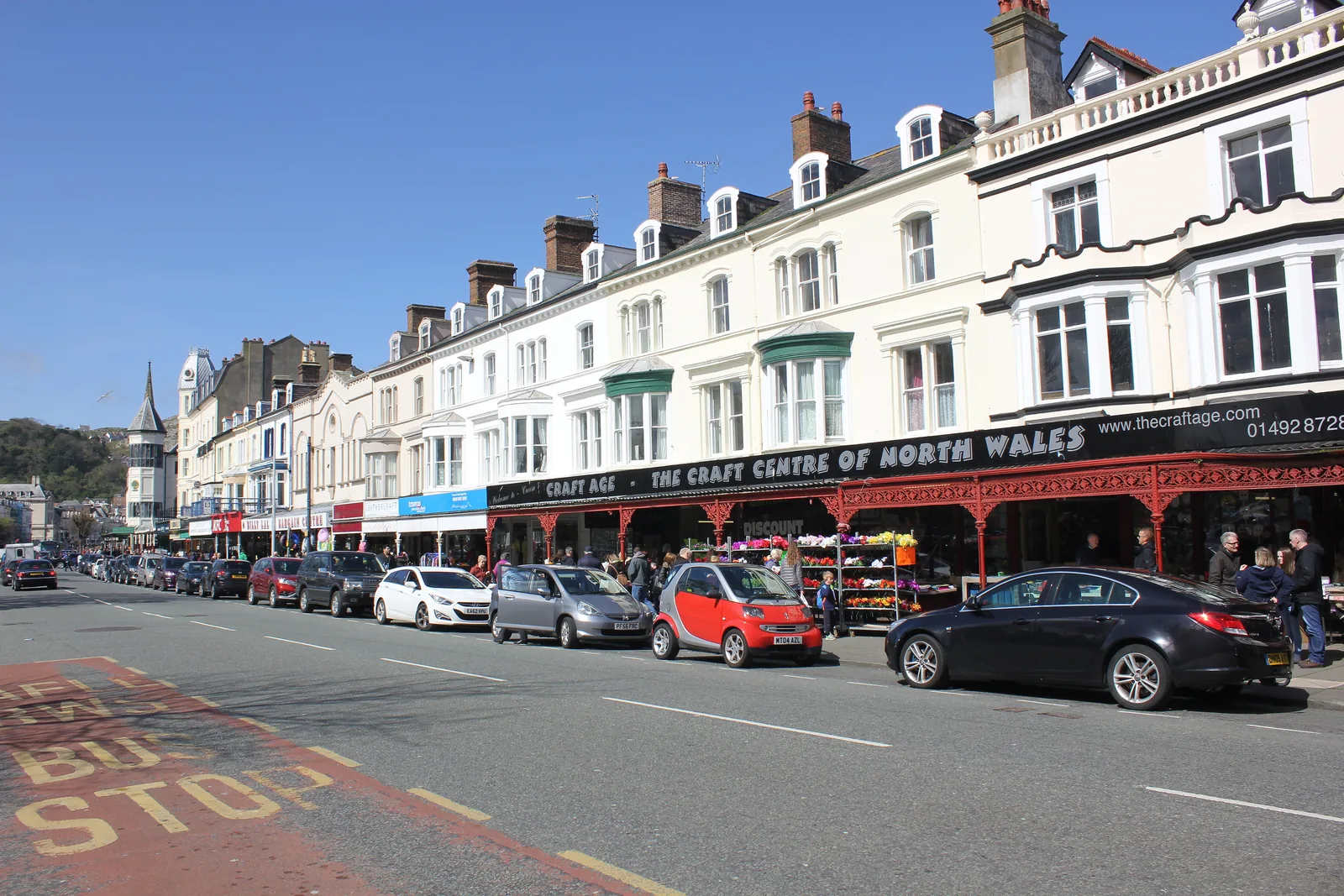 Shopfronts and traffic along Mostyn Street, Llandudno, terraced upper storeys above a canopied craft centre