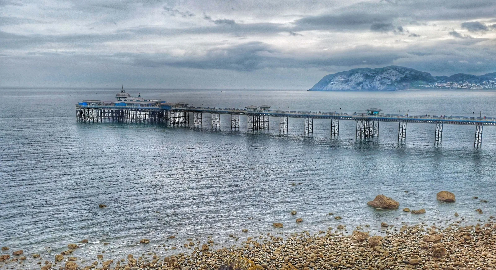 Llandudno Pier reaching out over calm water at dusk, the Little Orme dark on the far side of the bay
