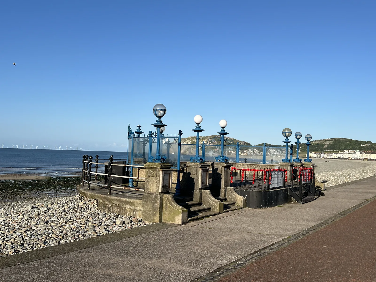 Ornate blue and red cast-iron promenade ironwork at Llandudno, the bay on one side and the Great Orme rising behind