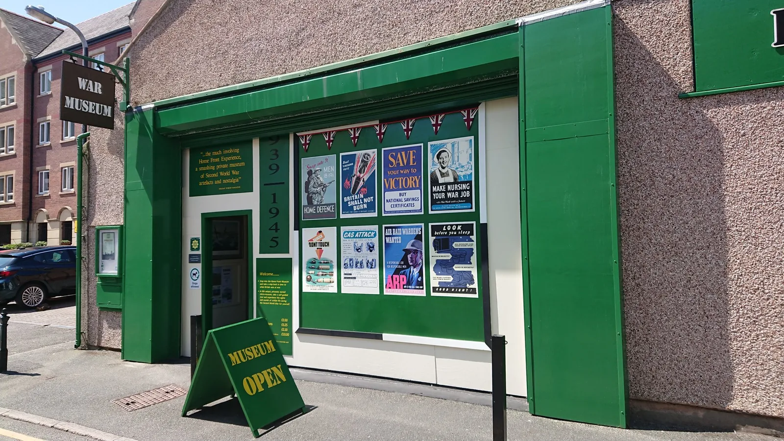 The green shopfront of the Home Front Museum on New Street, Llandudno, hung with wartime posters beside a Museum Open board