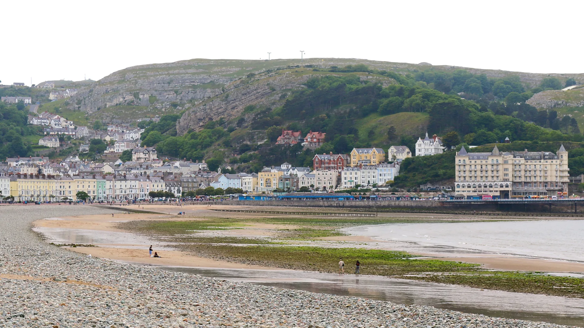 The curve of Llandudno Bay at low tide, pastel Victorian terraces and the Grand Hotel along the promenade with the Great Orme rising behind