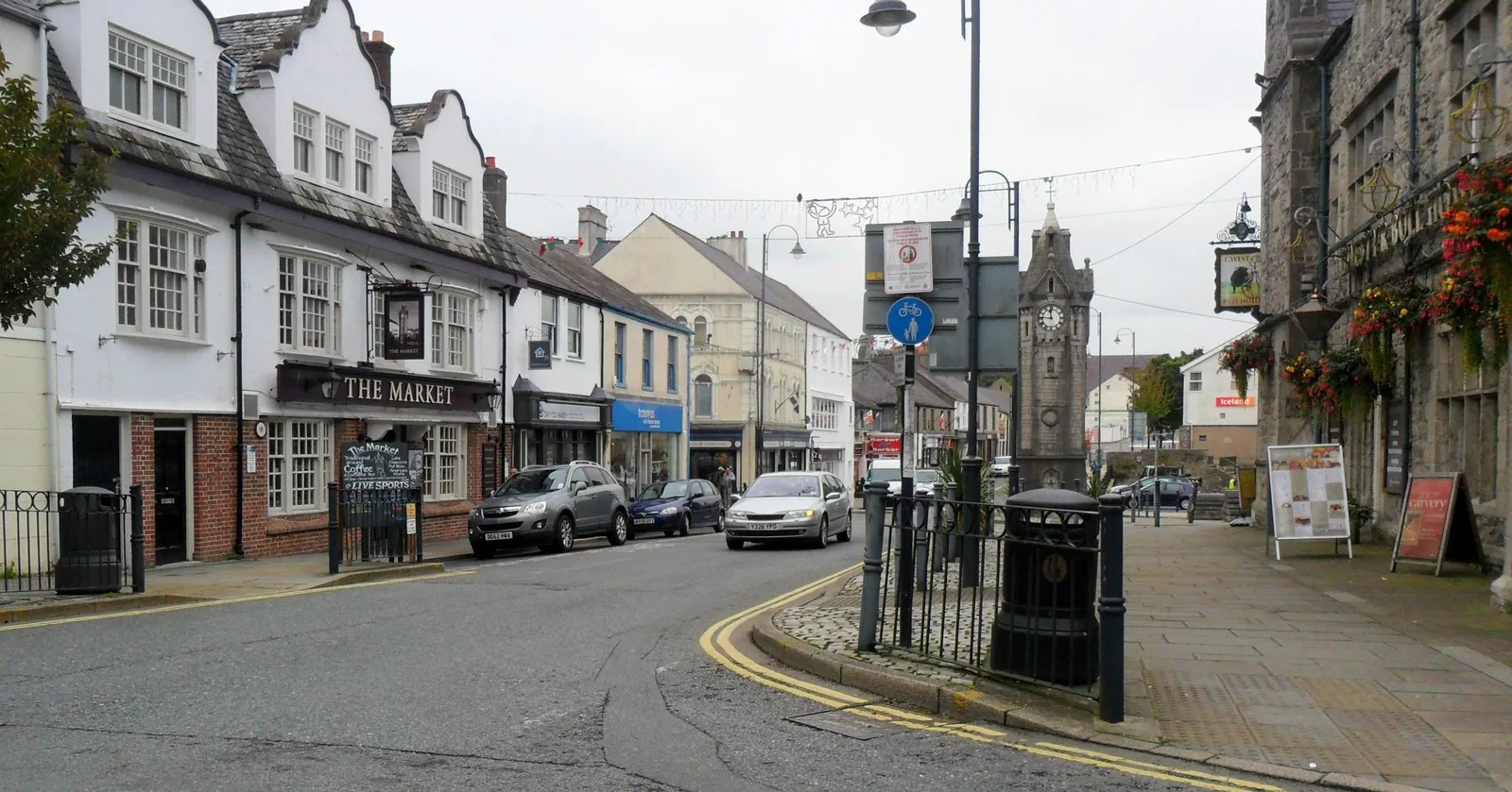 Llangefni High Street, painted shopfronts on one side and the stone town clock standing at the far end