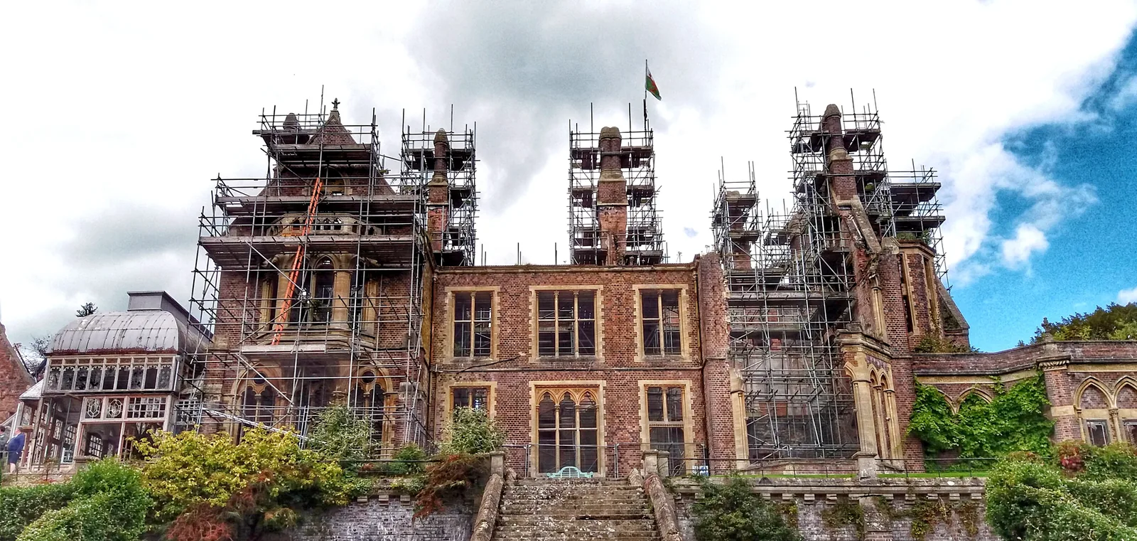 Hafodunos Hall, its Gothic Revival front wrapped in scaffolding, standing among trees in the valley west of Llangernyw