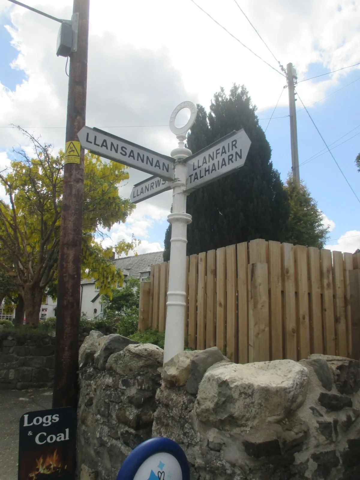 A bilingual fingerpost at Llangernyw, its arms lettered in Welsh and English above a stone wall