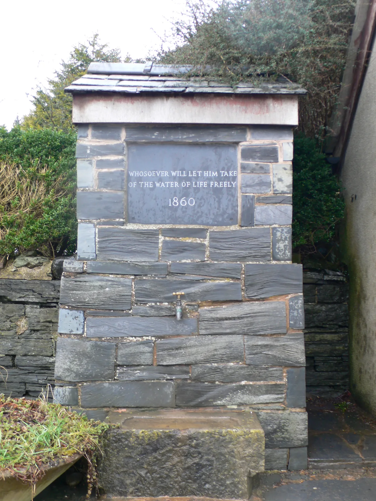 The village pump at Llangernyw, a slate structure with an inscribed panel and a planted stone trough