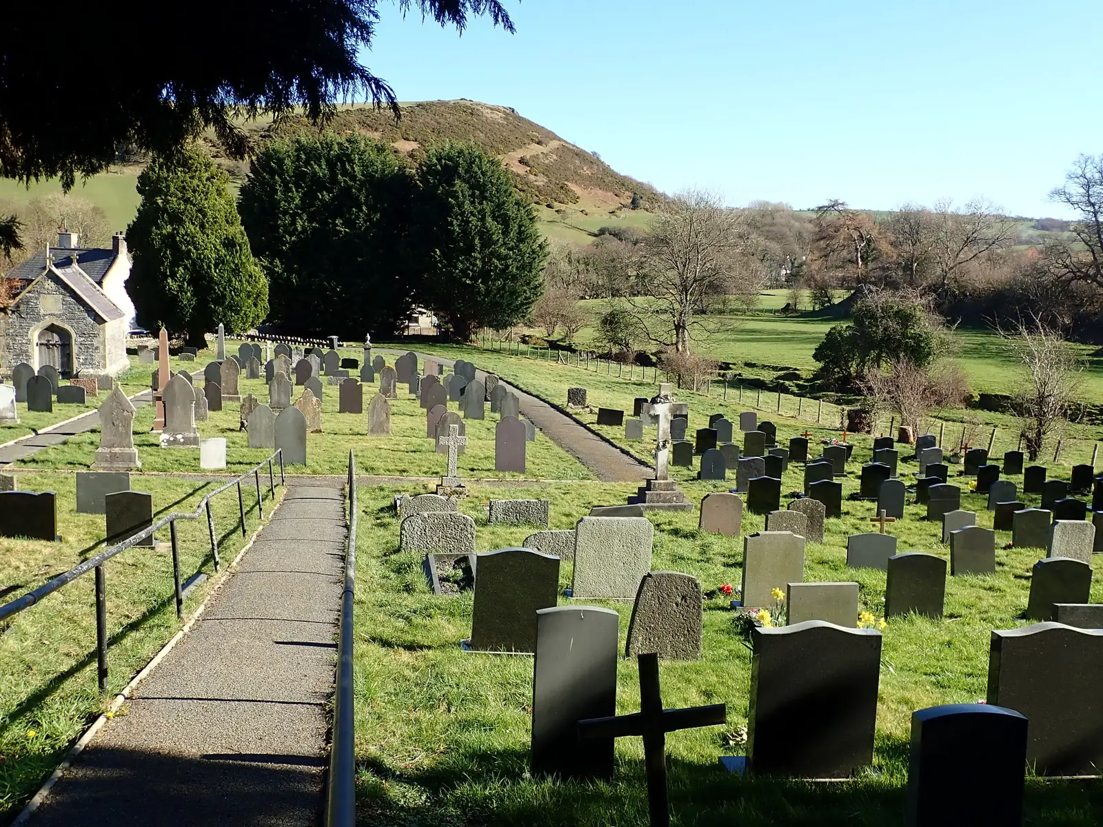 The cemetery at Llangernyw, rows of headstones on rising ground with a green hill behind