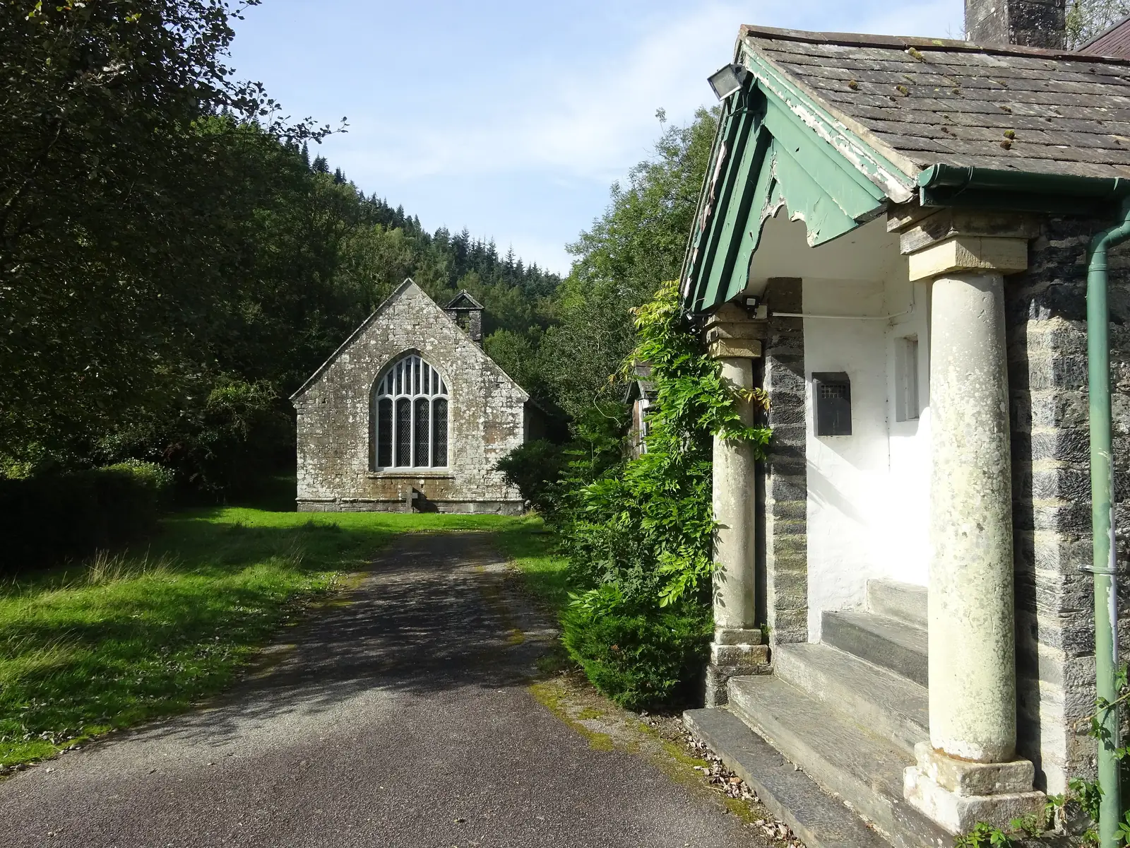 Gwydir Uchaf Chapel standing back from the track in its wooded setting above Gwydir Castle, its traceried west window facing the approach