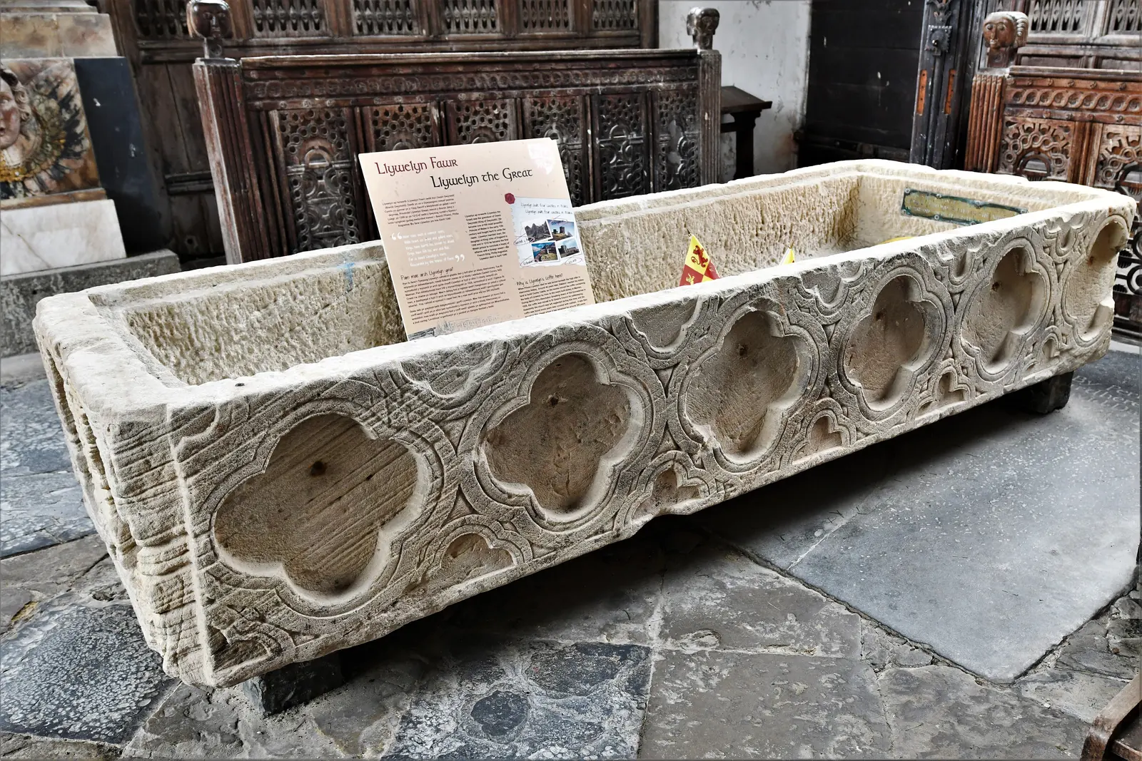 The carved 13th-century stone coffin in the Gwydir Chapel at Llanrwst, its side cut with quatrefoils, the chapel's dark carved woodwork behind
