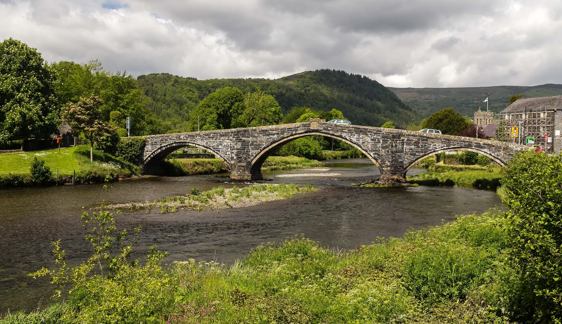 Pont Fawr's three stone arches spanning the River Conwy at Llanrwst, the wooded valley side rising behind