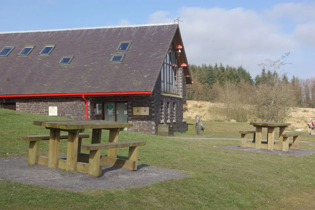 The Llyn Brenig Visitor Centre, a dark timber building with red trim and picnic tables outside.