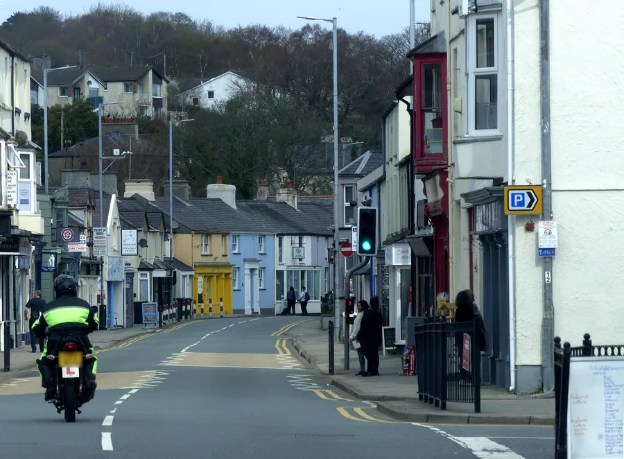 The High Street at Menai Bridge, shopfronts along both sides and people on the pavement.