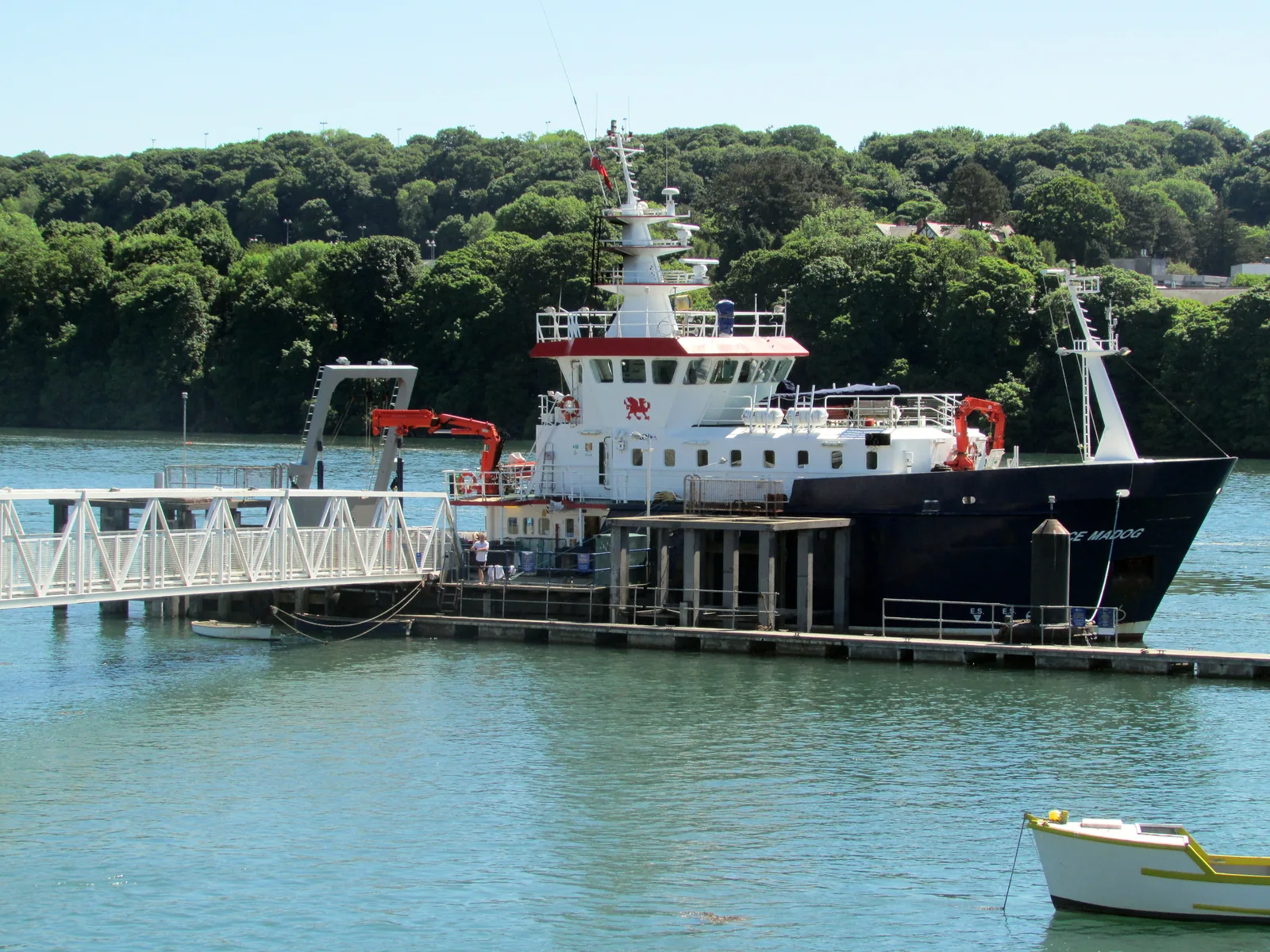 The research vessel Prince Madog moored alongside the landing stage at St George's Pier, Menai Bridge, with the wooded Gwynedd shore behind