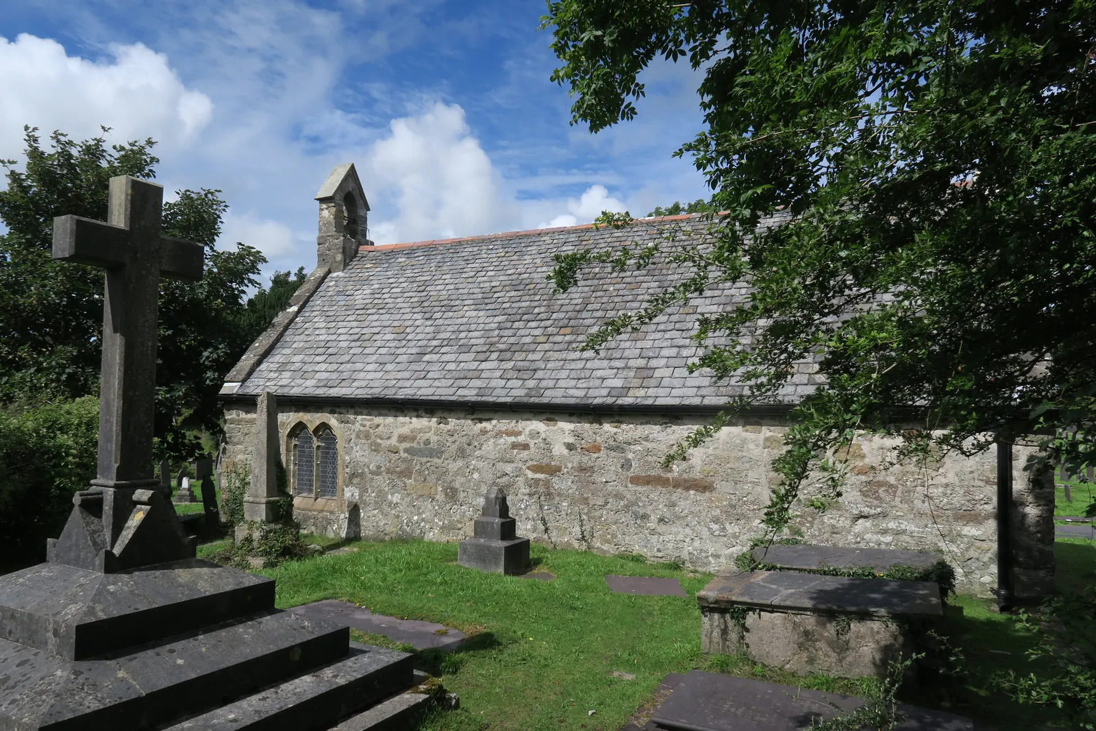 St Tysilio's Church on Church Island, Menai Bridge, its stone walls low behind a graveyard cross and headstones