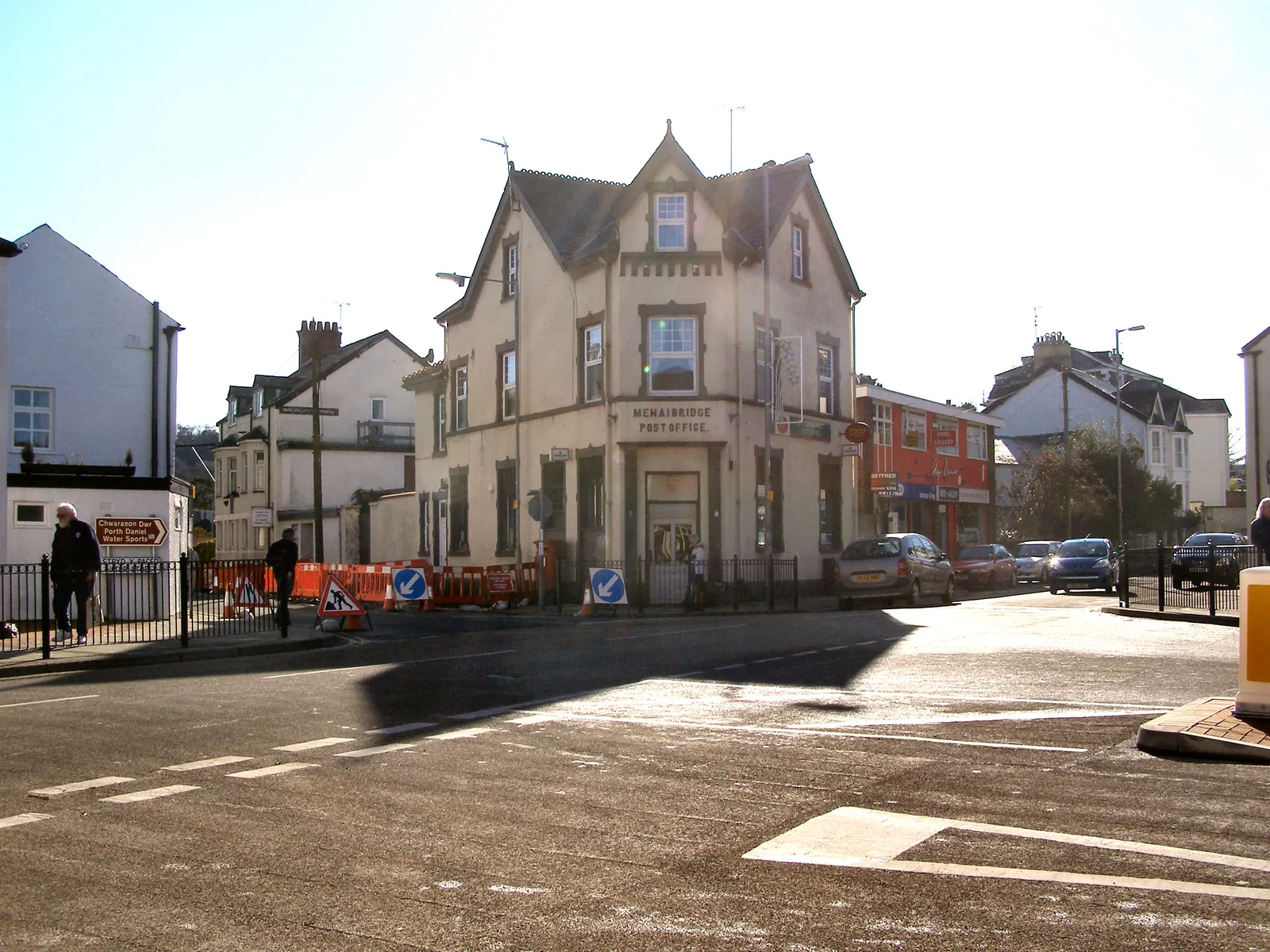 A street corner in the middle of Menai Bridge, roadworks barriers and parked cars in front of a large Victorian building