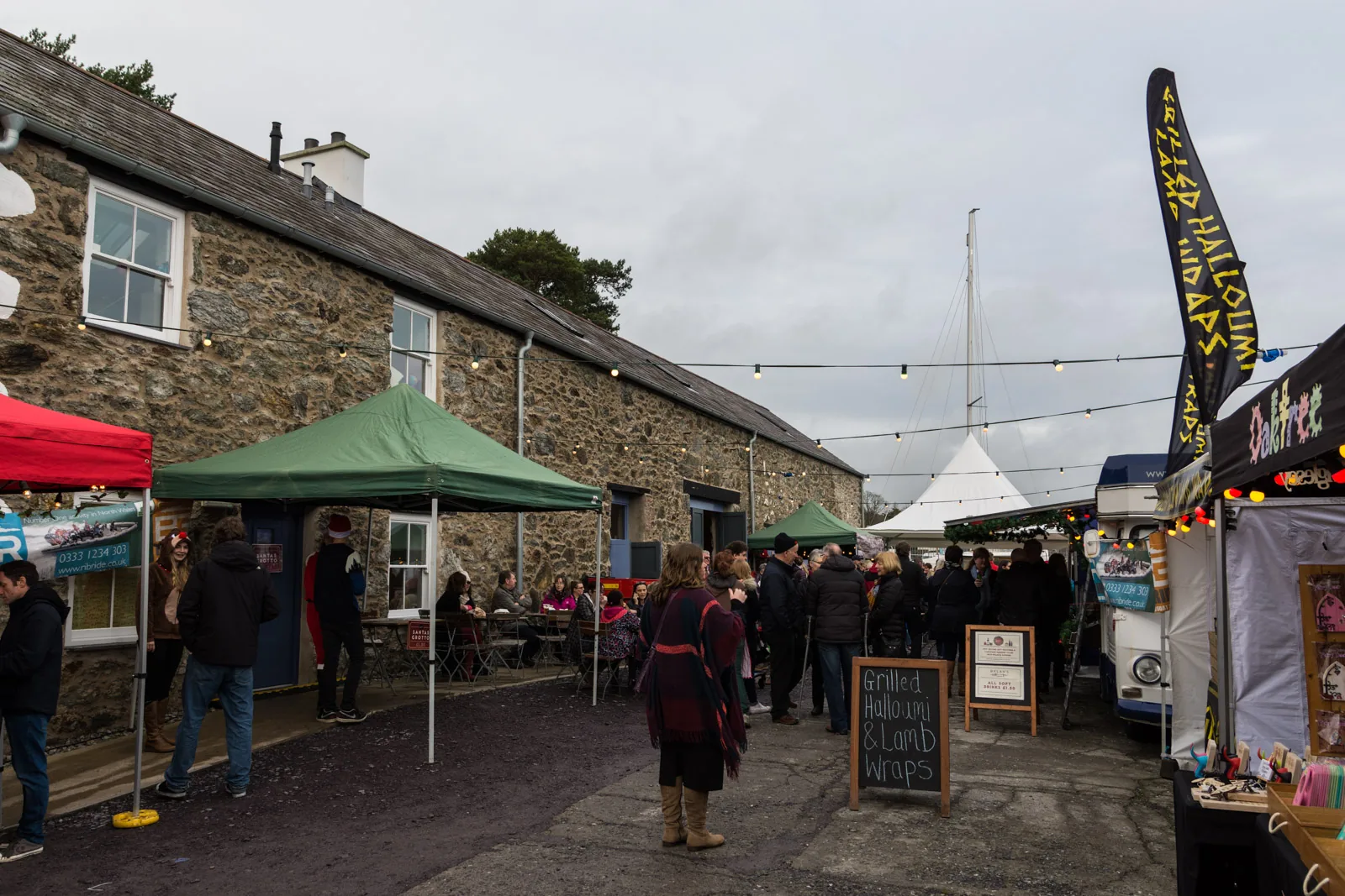 Stalls, gazebos and crowds along the stone building at Prince's Pier during a food festival at Menai Bridge