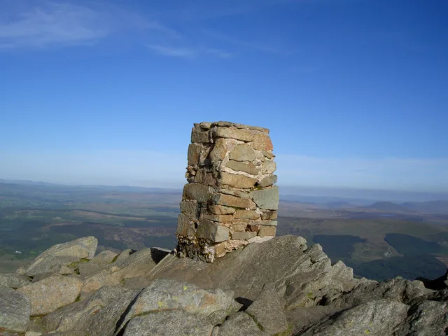The stone trig point on the summit of Moel Siabod, standing on bare rock with a hazy panorama of Eryri behind