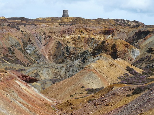 The Great Opencast at Parys Mountain: a vast open copper pit with mineral-stained rock faces in ochre, rust and deep red, viewed from the ridge path.