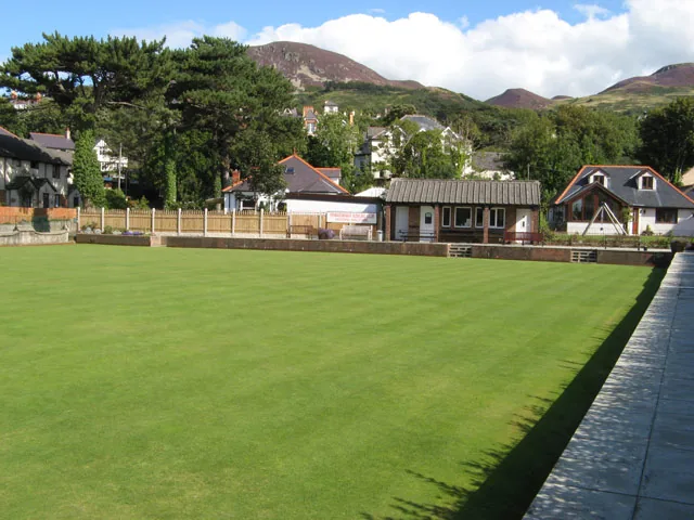 A closely mown bowling green at Penmaenmawr with the flank of the mountain rising behind the trees