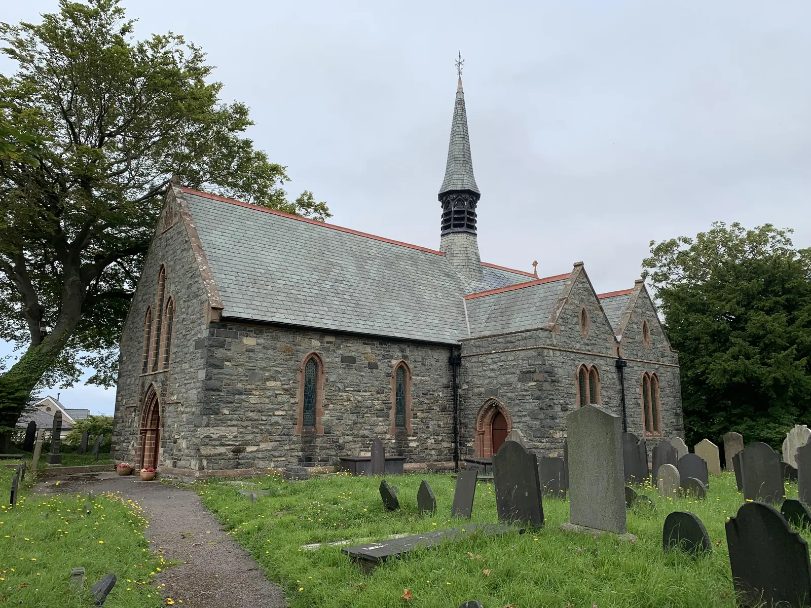 The parish church at Dwygyfylchi, a stone church with a slender spire standing among headstones