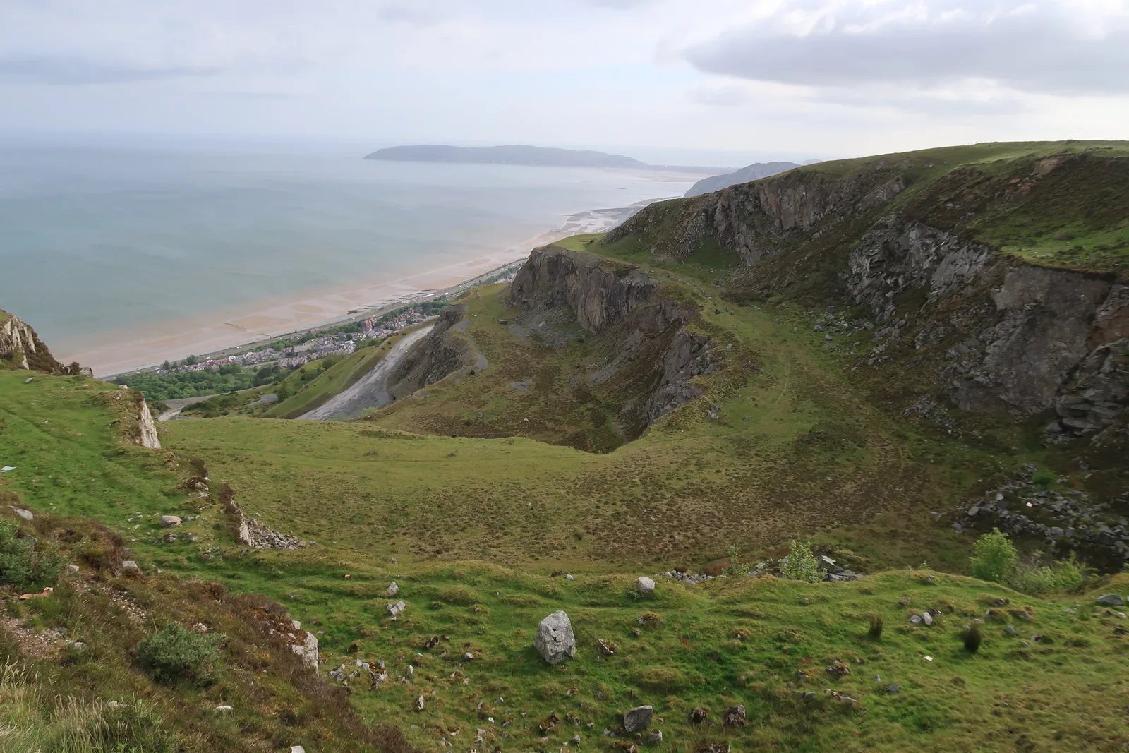 A grassed-over quarry hollow above Penmaenmawr, the coast and the beach curving away towards the Great Orme